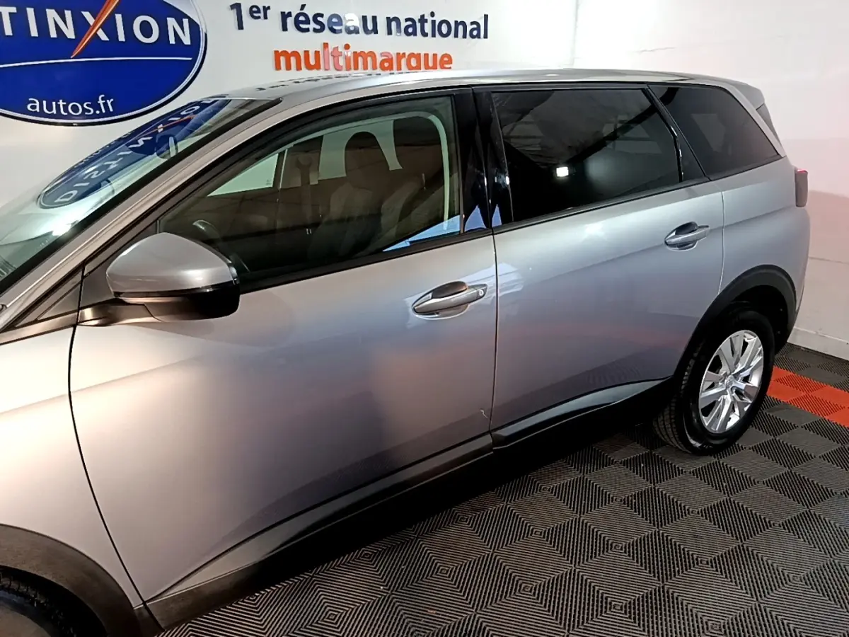 Vue latérale côté gauche d’un Peugeot 5008 gris clair, mettant en valeur ses portes et rétroviseur extérieur.