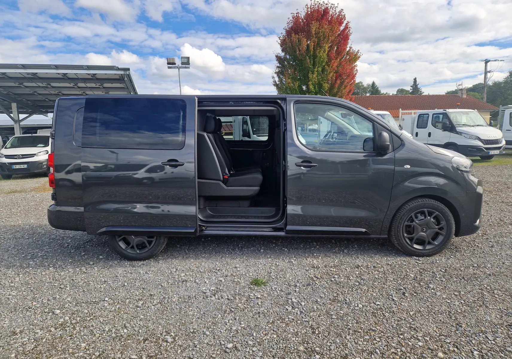 Profil droit du Citroën Jumpy XL gris titane avec porte coulissante ouverte révélant les sièges arrière.