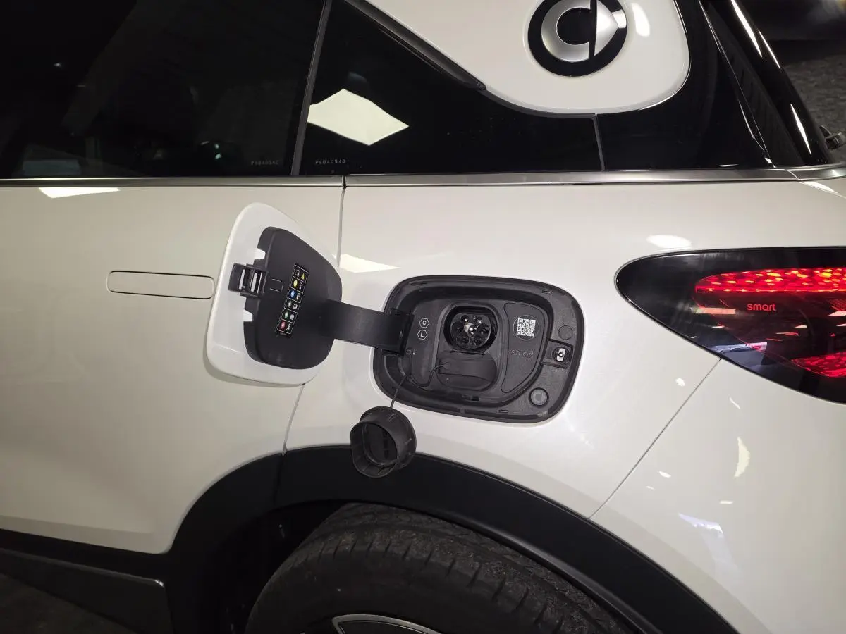 Prise de recharge électrique ouverte sur le côté gauche arrière d'une Smart #1 blanche avec feu arrière allumé.
