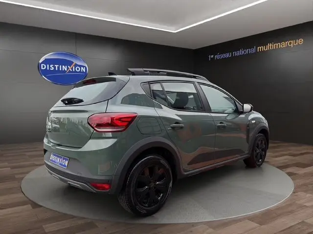 Vue 3/4 arrière droite d'une Dacia Sandero Stepway 2025 kaki lichen avec jantes noires et barres de toit.