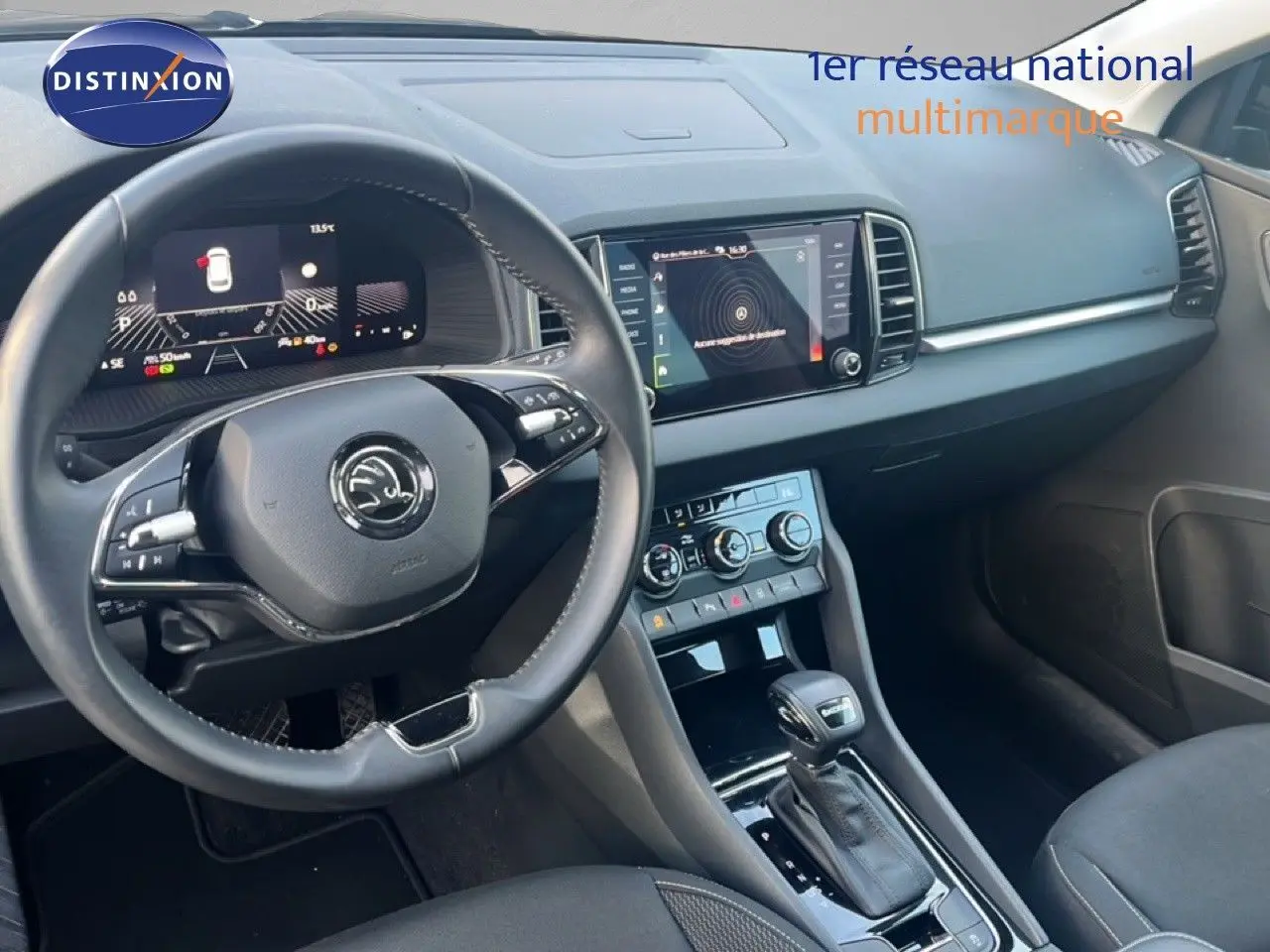 Vue intérieure du tableau de bord et volant du Skoda Karoq noir, avec écran tactile et commandes de climatisation visibles.