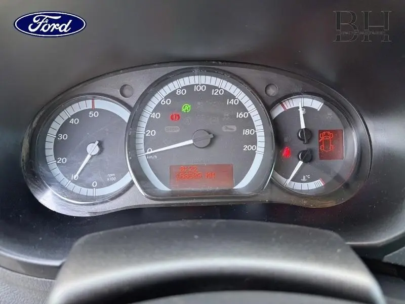 Tableau de bord vu de face avec compteurs analogiques et écran digital, affichage de vitesse et jauges, intérieur noir.