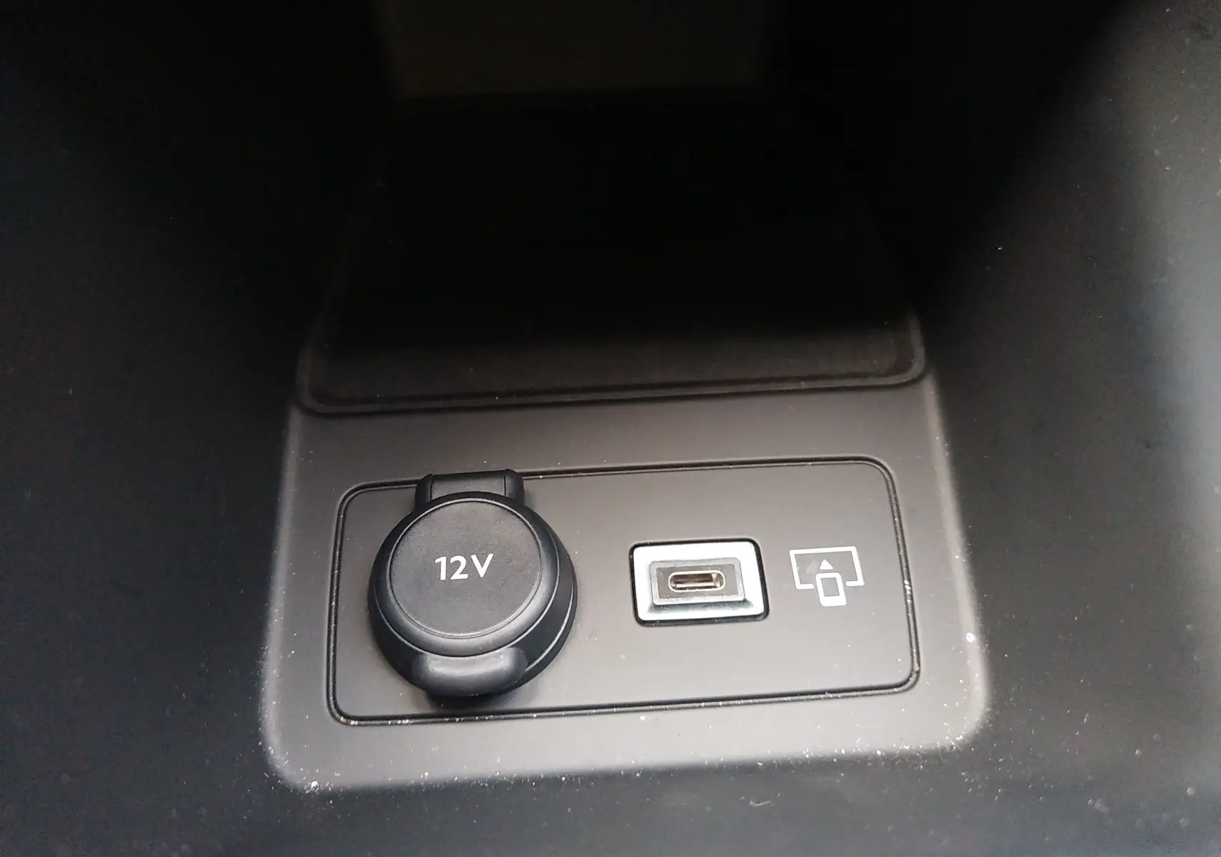 Prise 12V et port USB-C visibles dans le compartiment central de la Peugeot 408 Hybrid 2024 blanc Okenite.