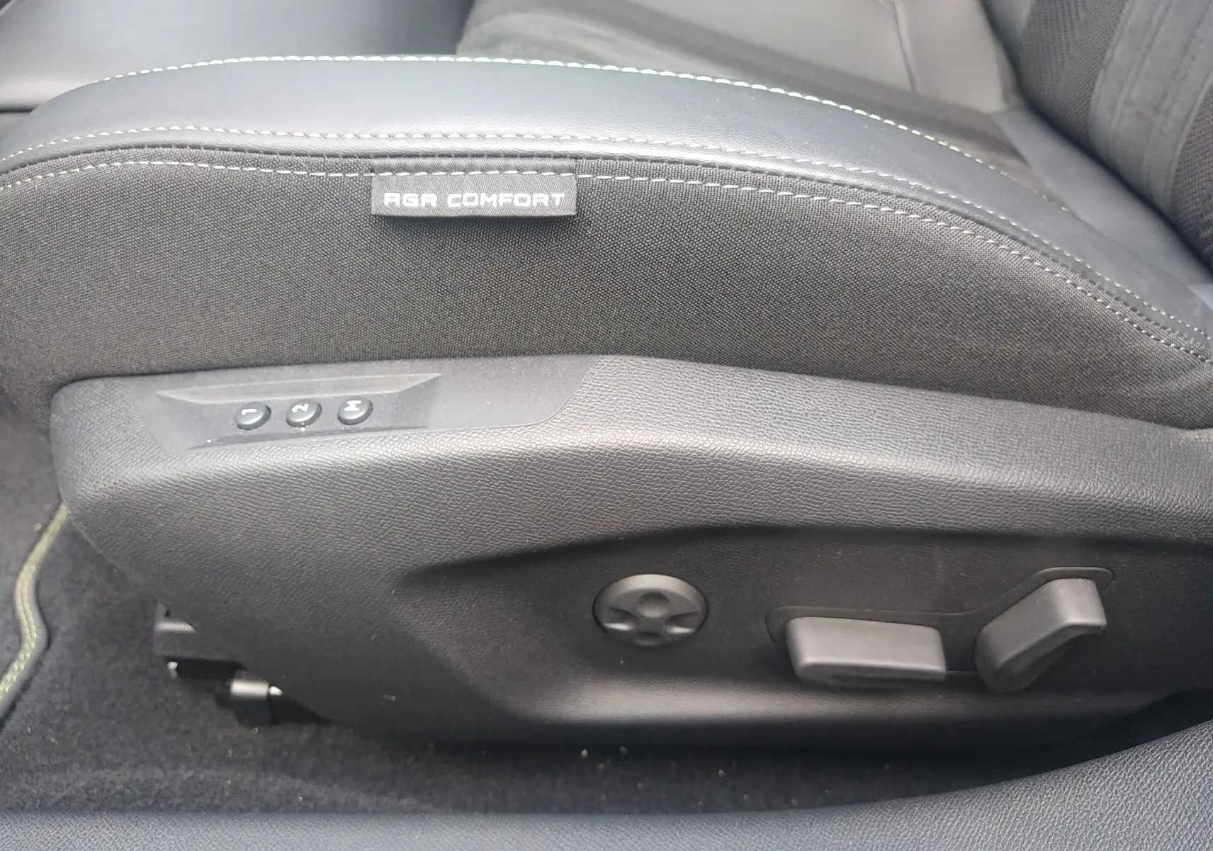 Détail du côté gauche du siège avant noir avec étiquette AGR Comfort et commandes de réglage électrique dans une Peugeot 408 Hybrid 2024.