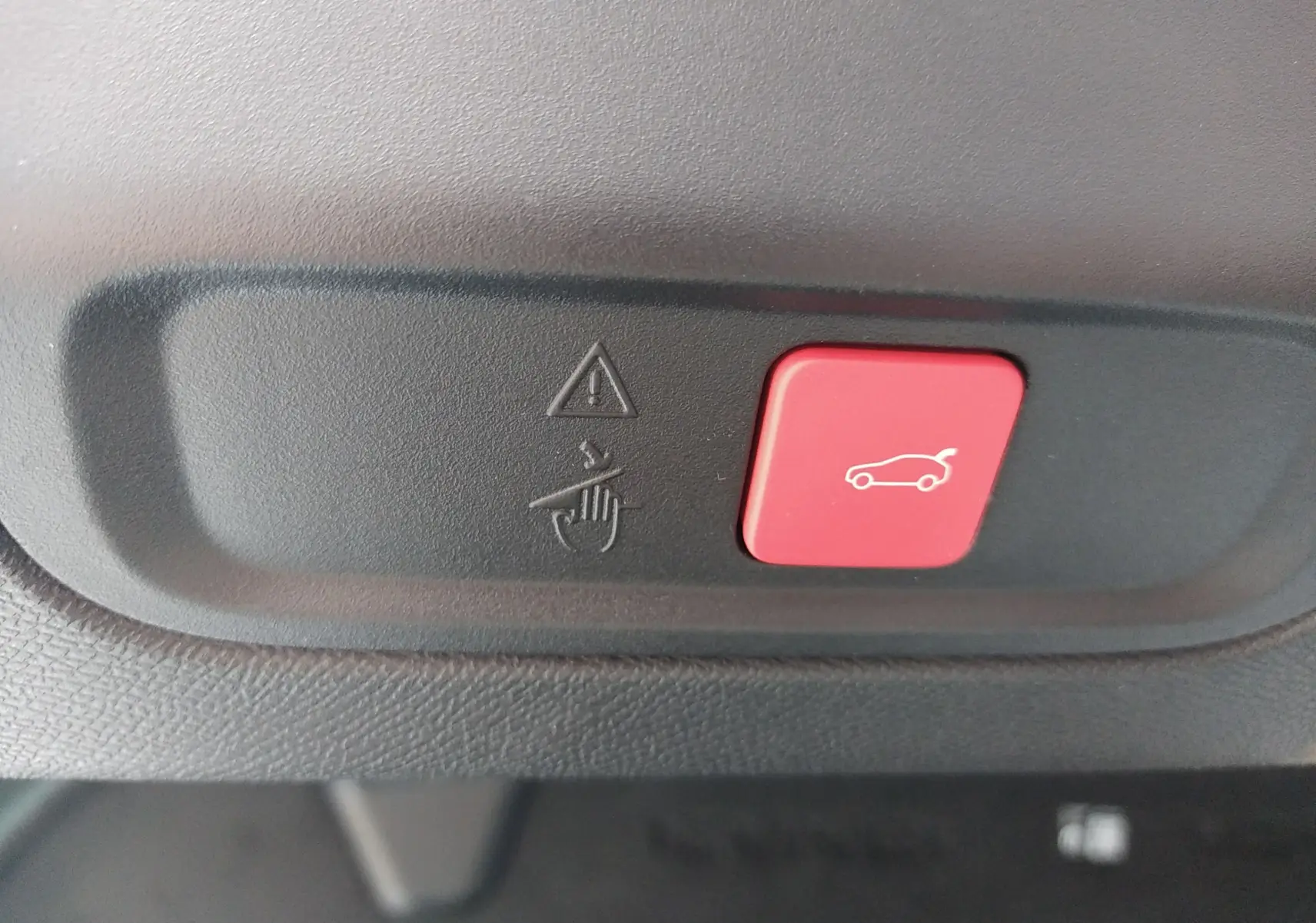 Bouton rouge de commande d'ouverture du coffre sur tableau de bord intérieur d'une Peugeot 408 blanche hybride 2024.