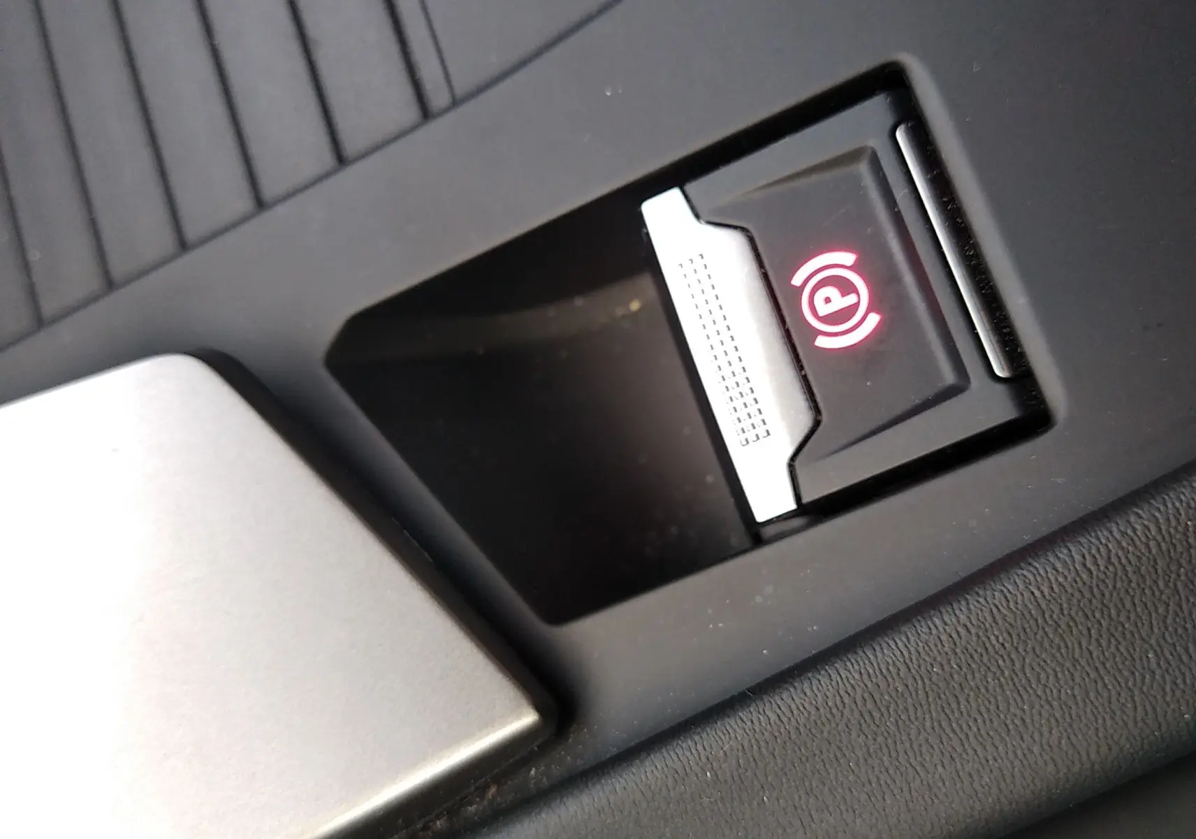 Gros plan sur le bouton de frein à main électronique rouge dans l'habitacle noir du Peugeot 408 Hybrid 2024.