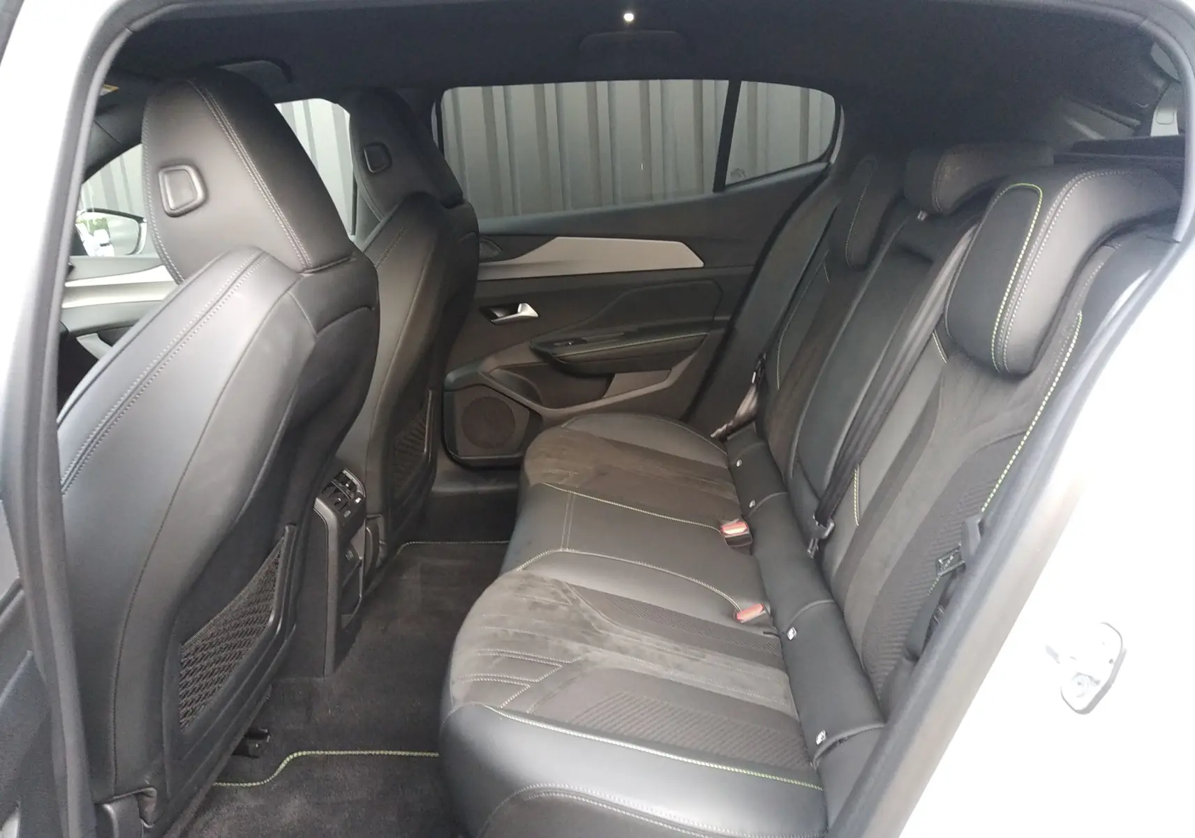 Vue intérieure côté droit des sièges arrière en cuir noir avec surpiqûres vertes d'une Peugeot 408 Hybrid 2024 blanc Okenite.