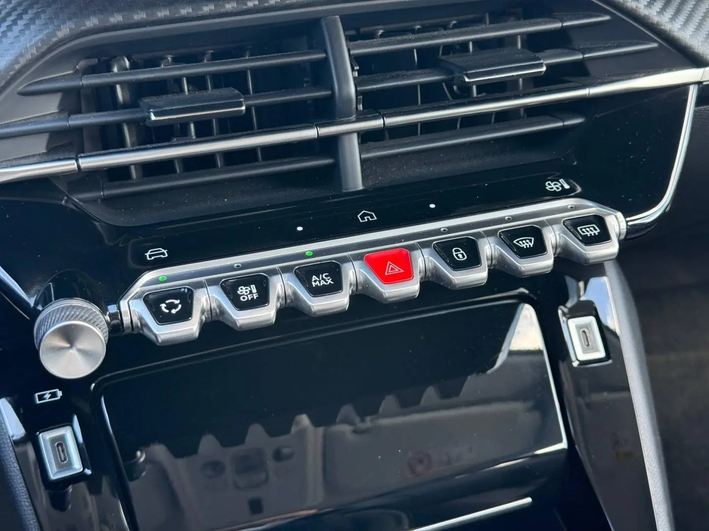 Vue rapprochée de la console centrale noire brillante de la Peugeot 208 1.2 100ch Allure avec boutons argentés et rouge d’alerte.