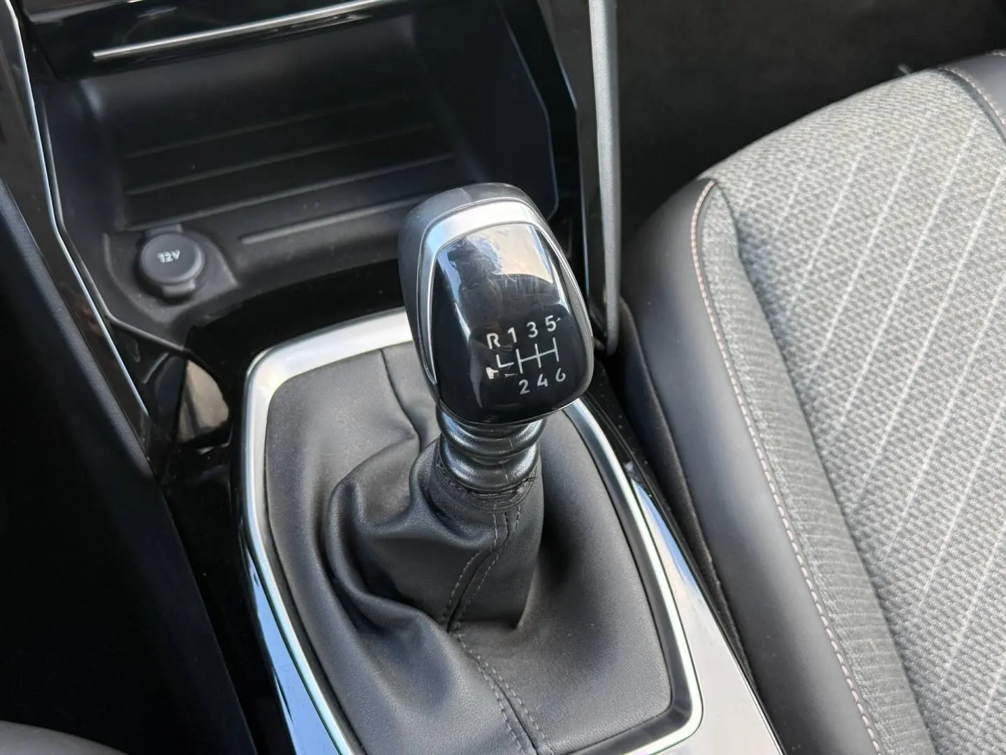 Le levier de vitesses manuel noir de la Peugeot 208 1.2 100ch Allure, avec sellerie tissu gris à motifs.