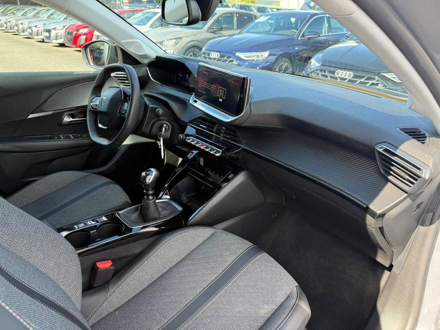Vue intérieure côté passager de la Peugeot 208 2025 avec sellerie tissu gris et tableau de bord moderne noir.