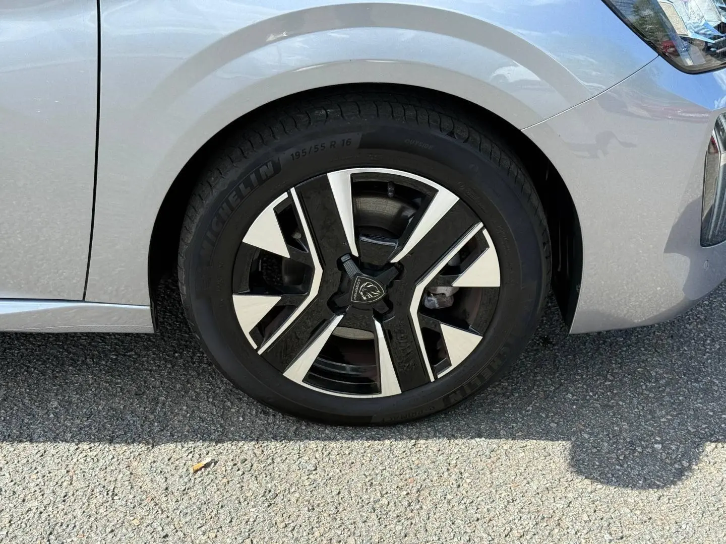 Gros plan sur la roue avant droite d'une Peugeot 208 2025 gris Artense avec jante alu bicolore moderne.