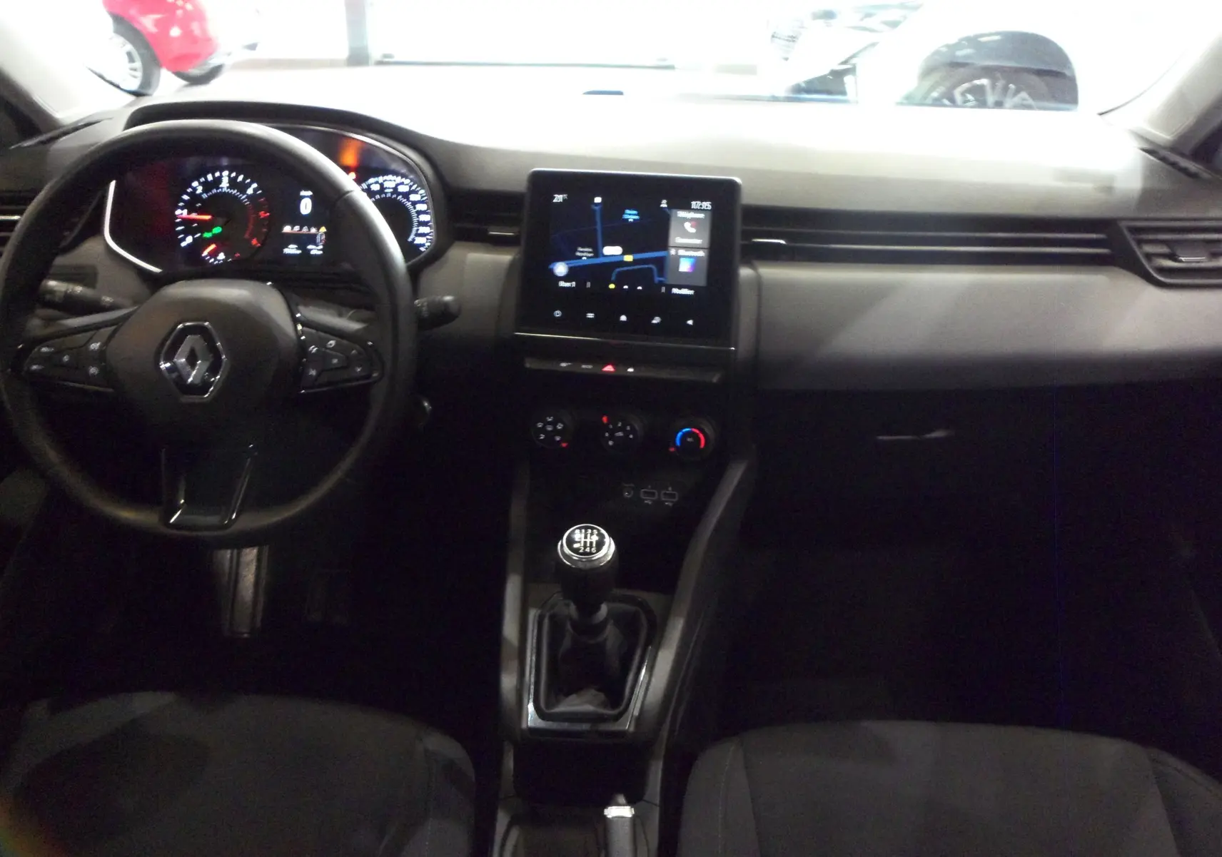 Vue intérieure centrée sur le tableau de bord et la console centrale d'une Renault Clio V blanche avec boîte manuelle.