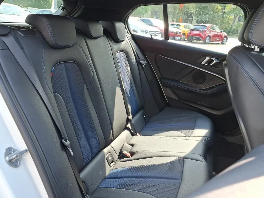 Vue intérieure sur les sièges arrière en cuir noir de la BMW Série 1 blanche, avec détails sport et habillage de porte visible.