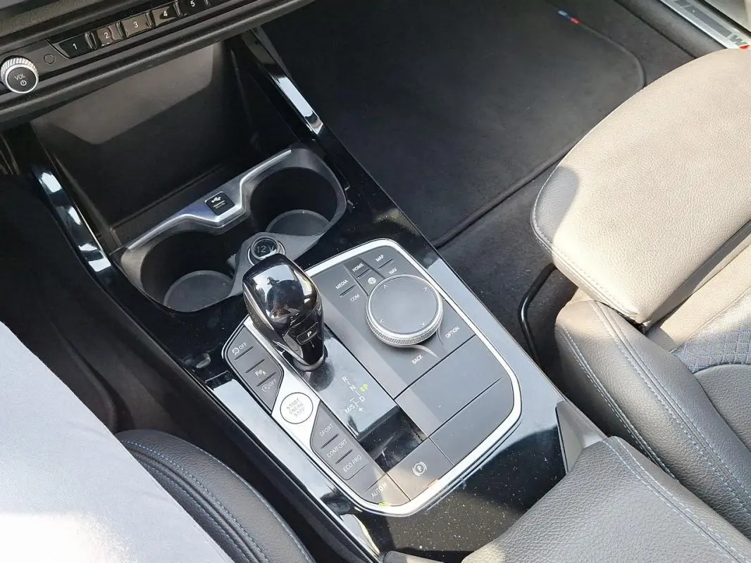 Gros plan sur la console centrale noire brillante de la BMW Série 1 120i M Sport avec levier de vitesse automatique et accoudoir cuir beige.