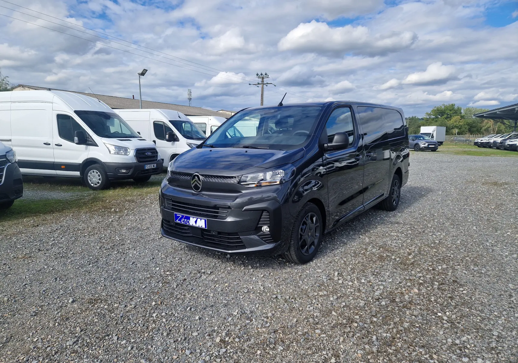 Citroën Jumpy Cabine Approfondie gris titane vu en 3/4 avant droit sur un parking extérieur avec plusieurs fourgons blancs.