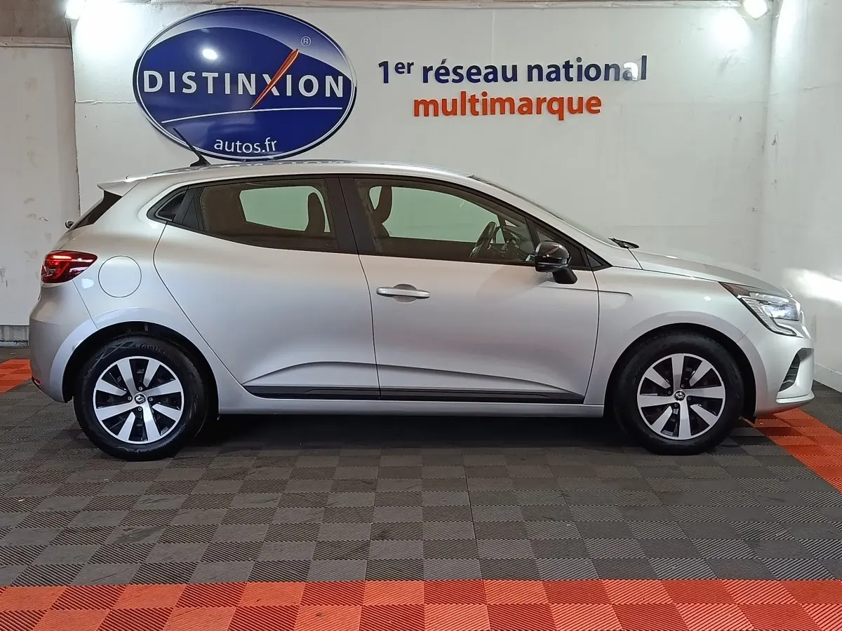 Profil droit d'une Renault Clio gris clair 2023, avec jantes alliage et rétroviseurs noirs dans un showroom.