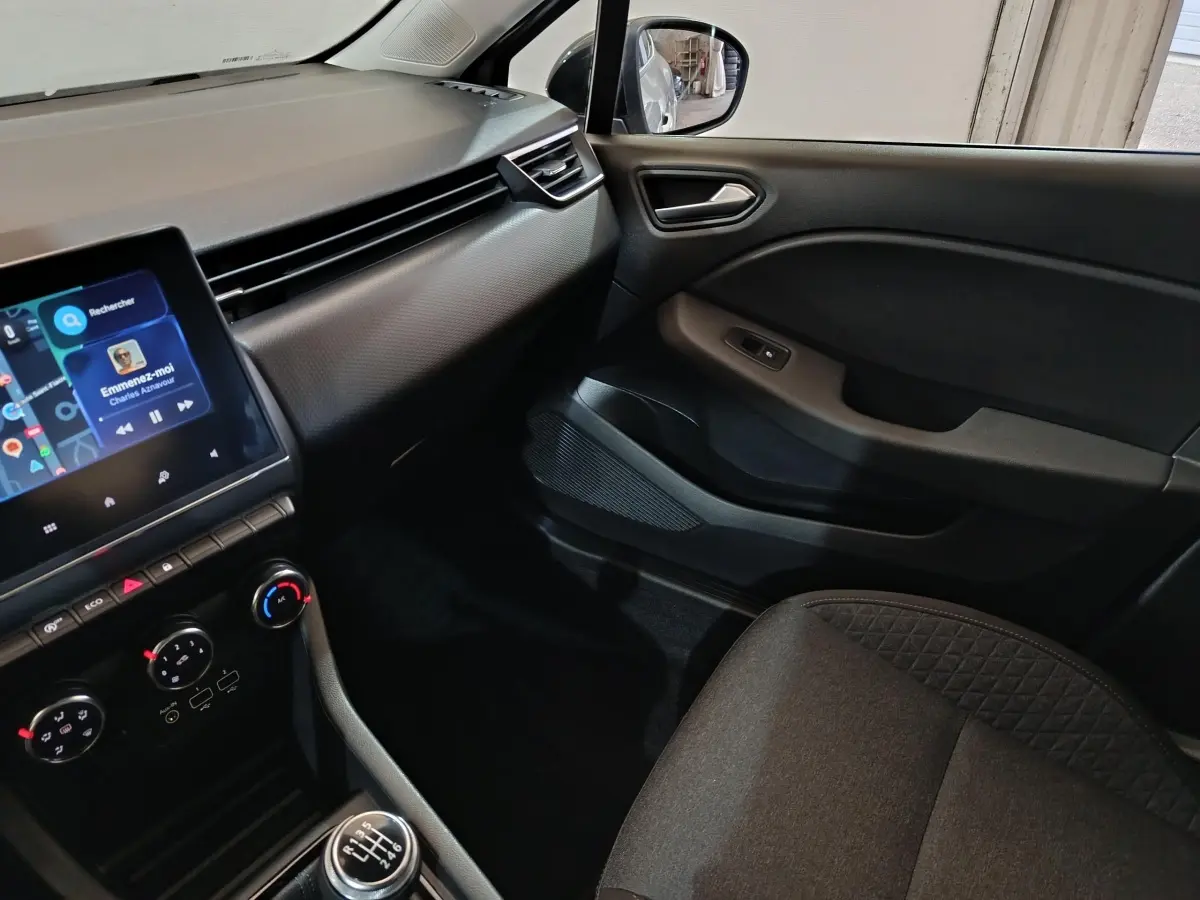 Vue intérieure côté passager de la Renault Clio gris clair 2023, avec écran tactile et console centrale manuelle.