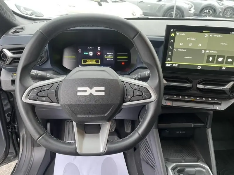Vue intérieure centrée sur le volant multifonction du Dacia Duster 2025 gris schiste avec tableau de bord digital et écran tactile.