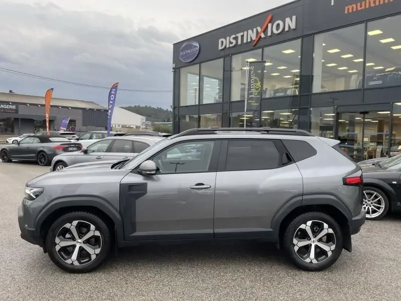 Vue de profil côté gauche du Dacia Duster 1.6 Hybrid gris schiste 2025 avec jantes distinctives et toit noir.