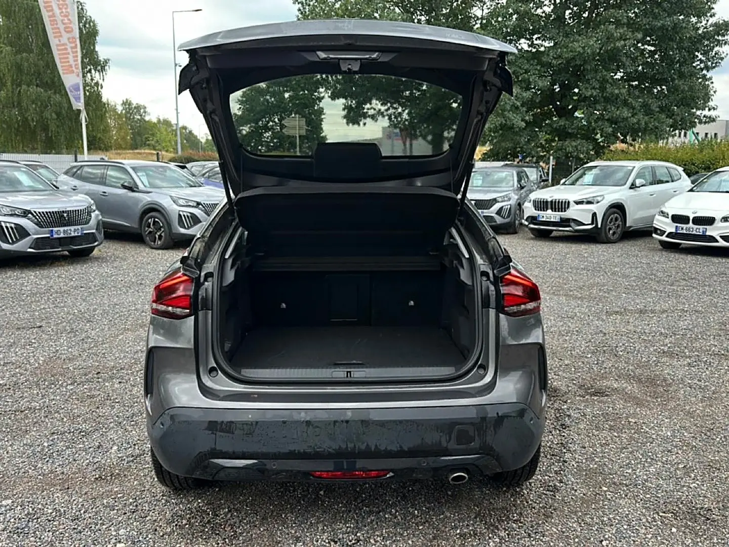 Vue arrière d'une Citroën C4 gris métallisé 2024 avec coffre ouvert sur un parking extérieur.