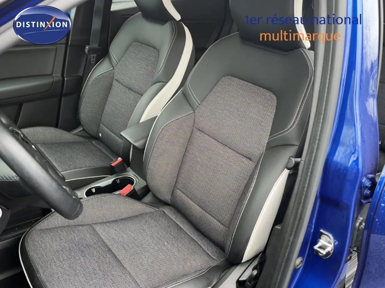 Vue intérieure côté conducteur du Renault Captur bleu iron metal, mettant en valeur les sièges tissu et cuir noir avec surpiqûres blanches.