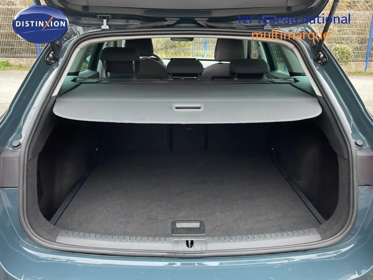 Coffre ouvert vu de l'arrière d'une SEAT LEON ST 2025 bleu Fjord, avec cache-bagages déployé et espace de chargement vide.