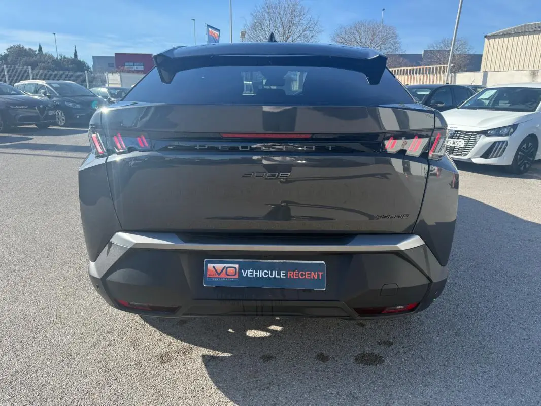 Vue arrière d’un Peugeot 3008 Hybrid gris 2025 avec feux arrière à griffes et logo Peugeot lumineux.