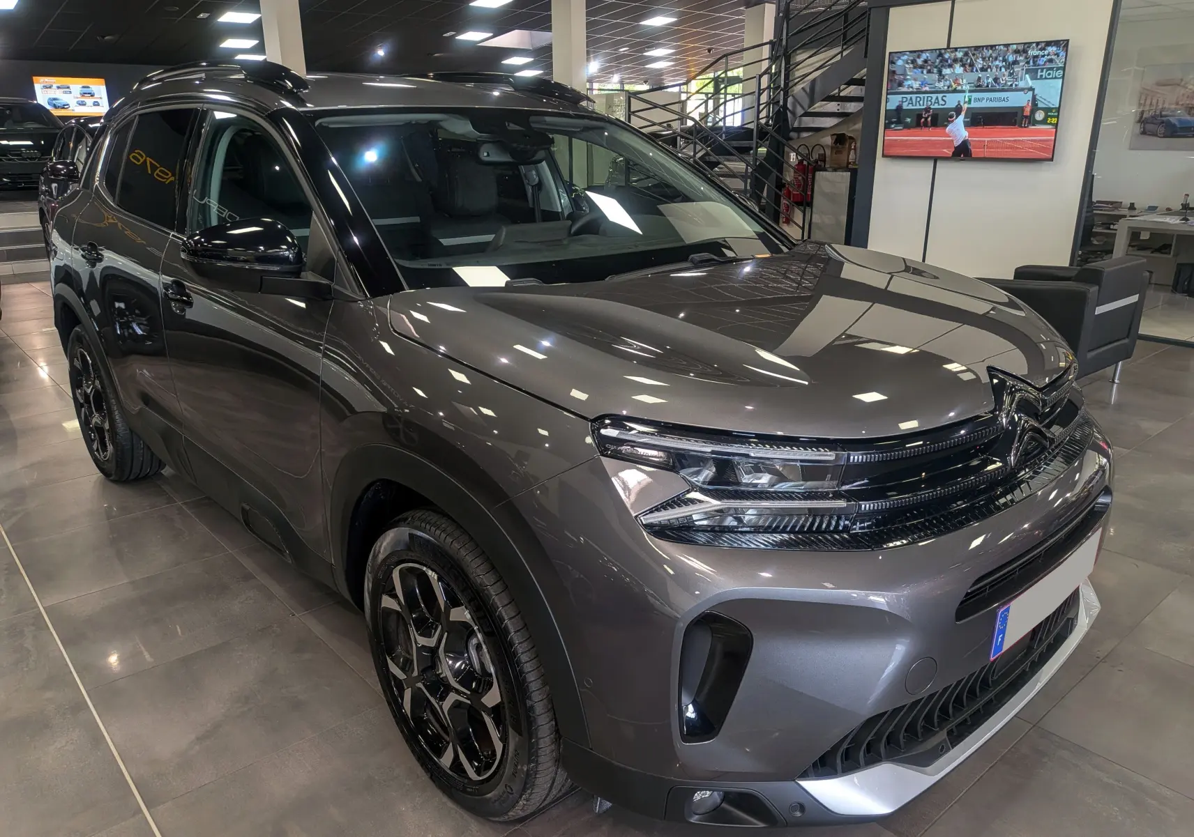 Vue 3/4 avant droite d'un Citroën C5 Aircross Hybride gris Platinium avec jantes noires biton dans un showroom.