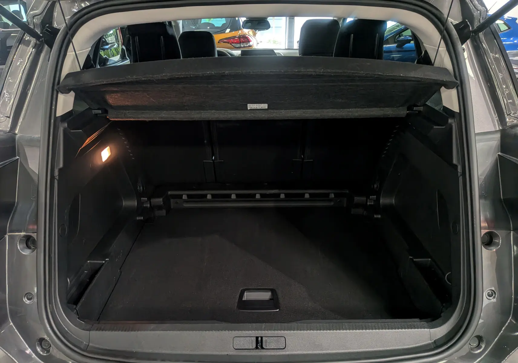 Coffre ouvert vu de l'arrière d'un Citroën C5 Aircross gris Platinium avec cache-bagages relevé et intérieur noir.