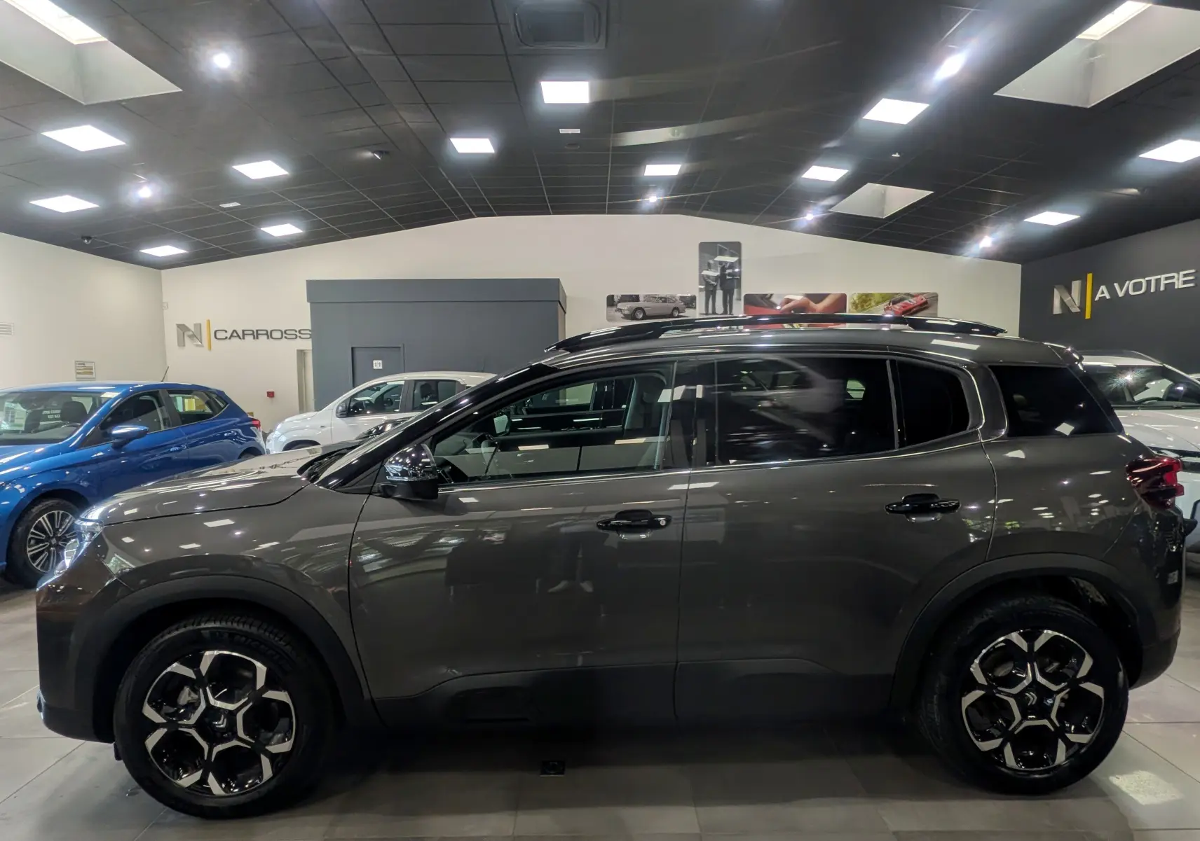 Vue de profil côté gauche du Citroën C5 Aircross Hybride gris Platinium avec jantes bi-ton en showroom.