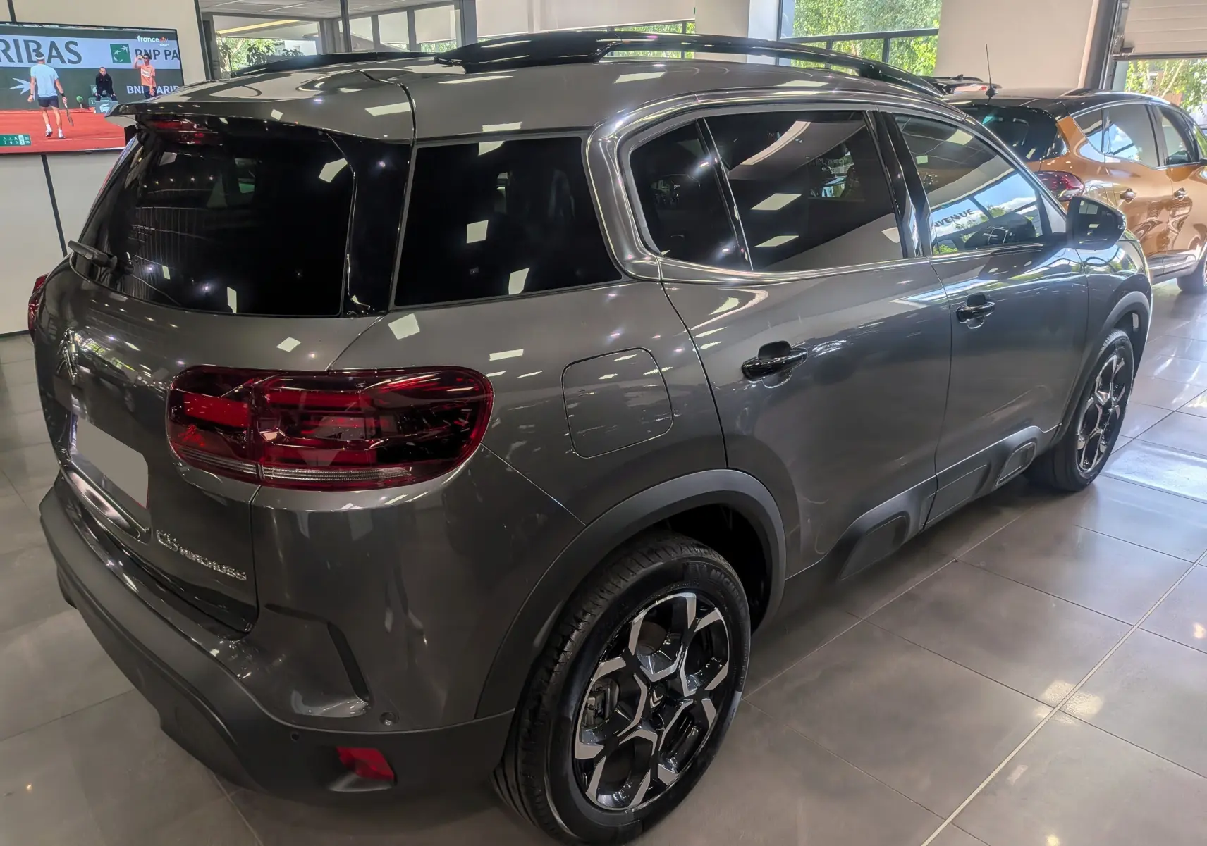 Vue 3/4 arrière droite du Citroën C5 Aircross Hybride gris Platinium avec toit noir et jantes bi-ton en showroom.