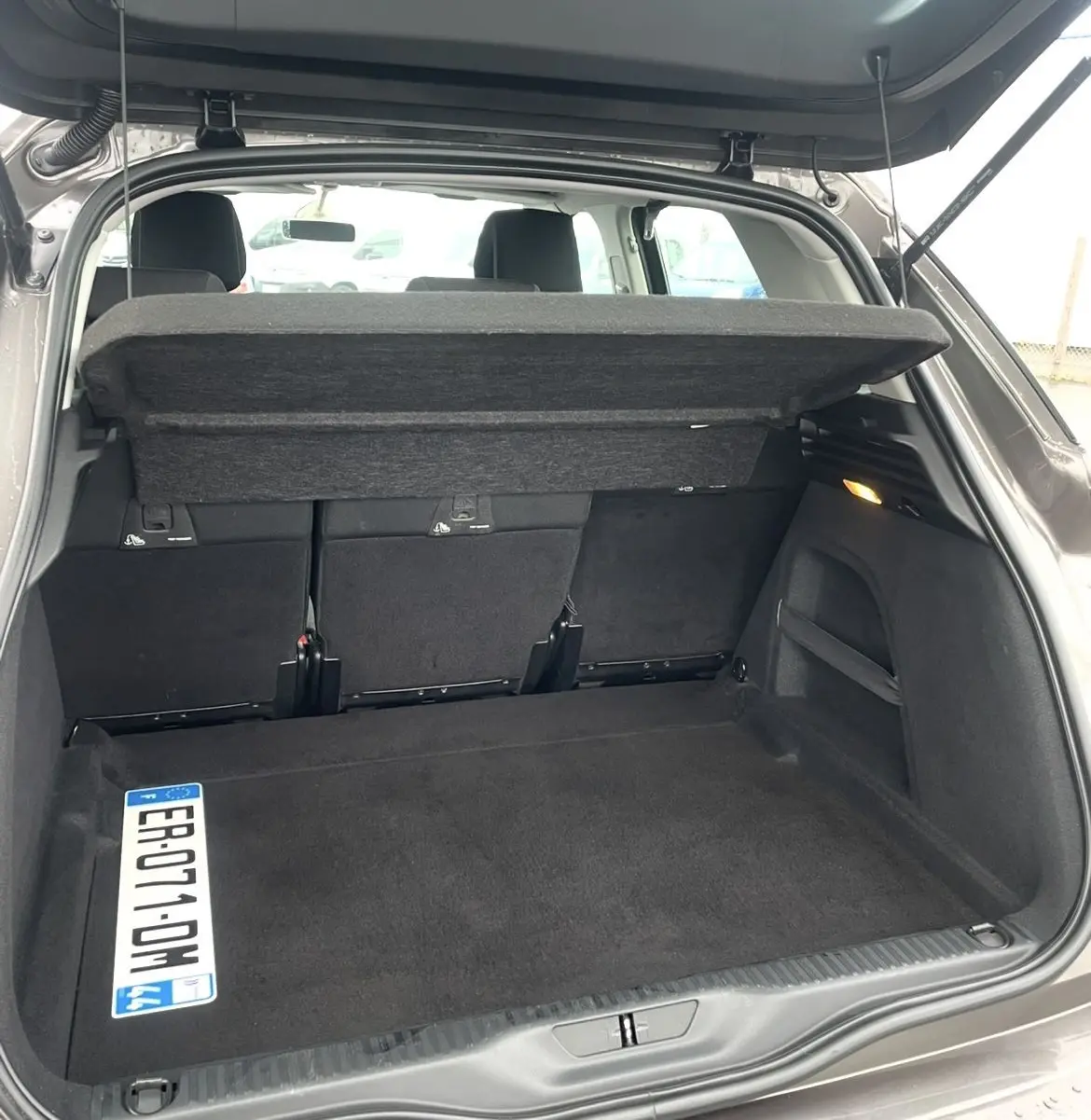 Coffre ouvert vu de l'arrière d'une Citroën C4 Picasso marron, avec cache-bagages relevé et banquette arrière visible.