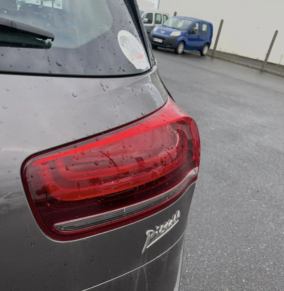 Gros plan sur le feu arrière droit d'une Citroën C4 Picasso marron sous la pluie, avec logo Picasso visible.