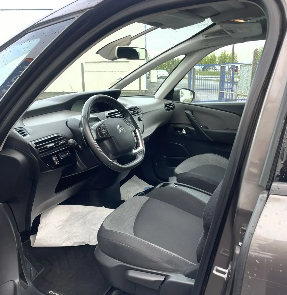 Vue intérieure côté conducteur du Citroën C4 Picasso marron 2017, volant cuir multifonction et sièges gris bi-ton.