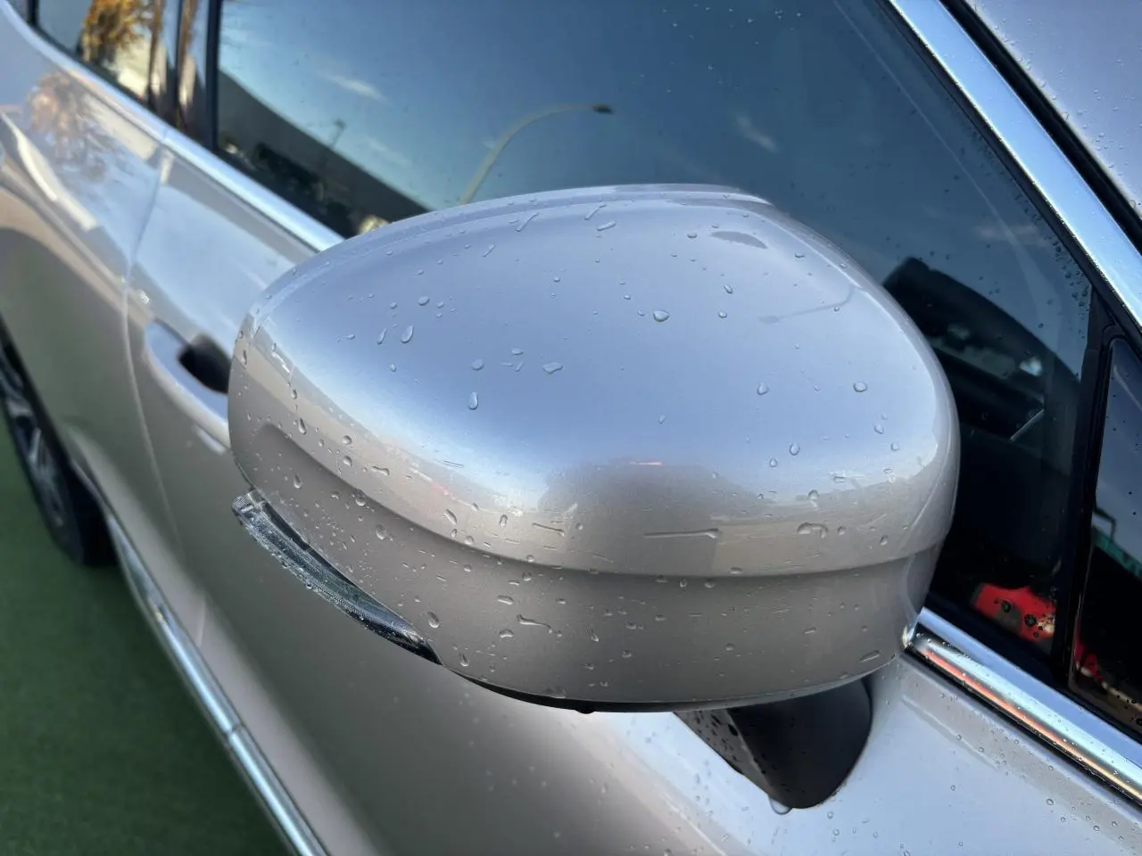 Rétroviseur côté gauche argent crépuscule métallisé du Volvo XC60 2024 avec gouttes d'eau et encadrement chromé.