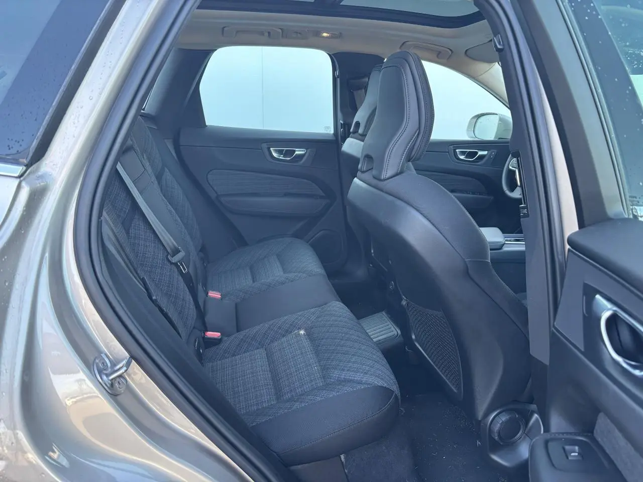 Vue intérieure côté gauche arrière du Volvo XC60 2024 argent crépuscule, sièges tissu gris à motifs et toit panoramique visible.