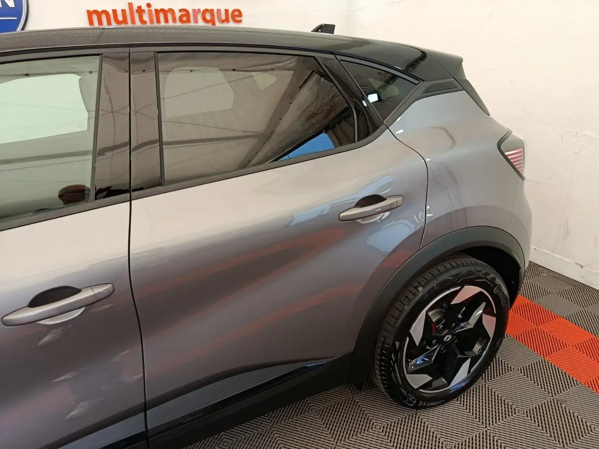 Vue côté droit arrière d'un Renault Captur gris foncé avec jante noire et toit noir dans un showroom.