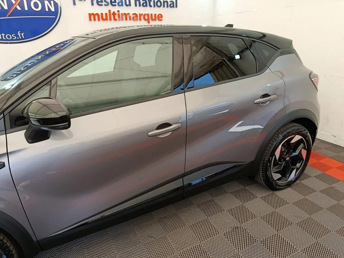 Profil côté gauche du Renault Captur gris foncé 2025 avec jantes noires et toit noir brillant visible en intérieur showroom