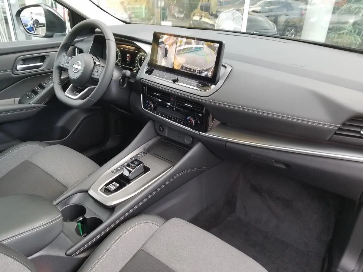 Vue intérieure avant droite du Nissan Qashqai 1.5 E-POWER 2025 avec écran tactile, volant multifonction et console moderne.