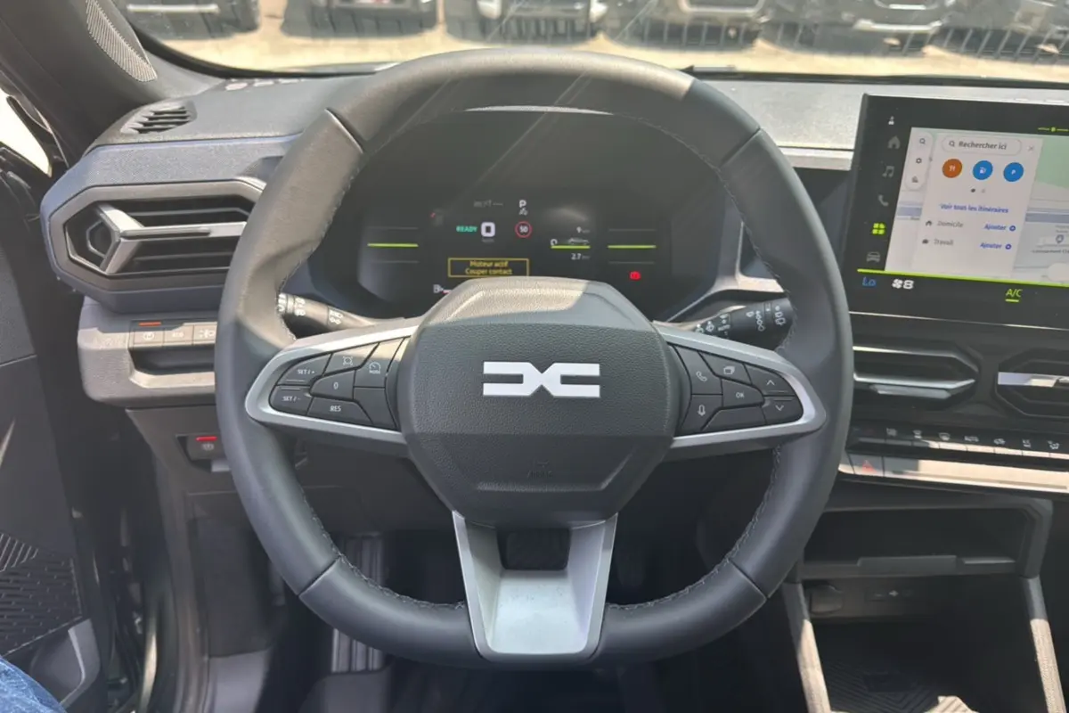 Vue intérieure centrée sur le volant cuir noir du Dacia Duster HEV 140 Journey Plus avec tableau de bord digital et écran tactile.