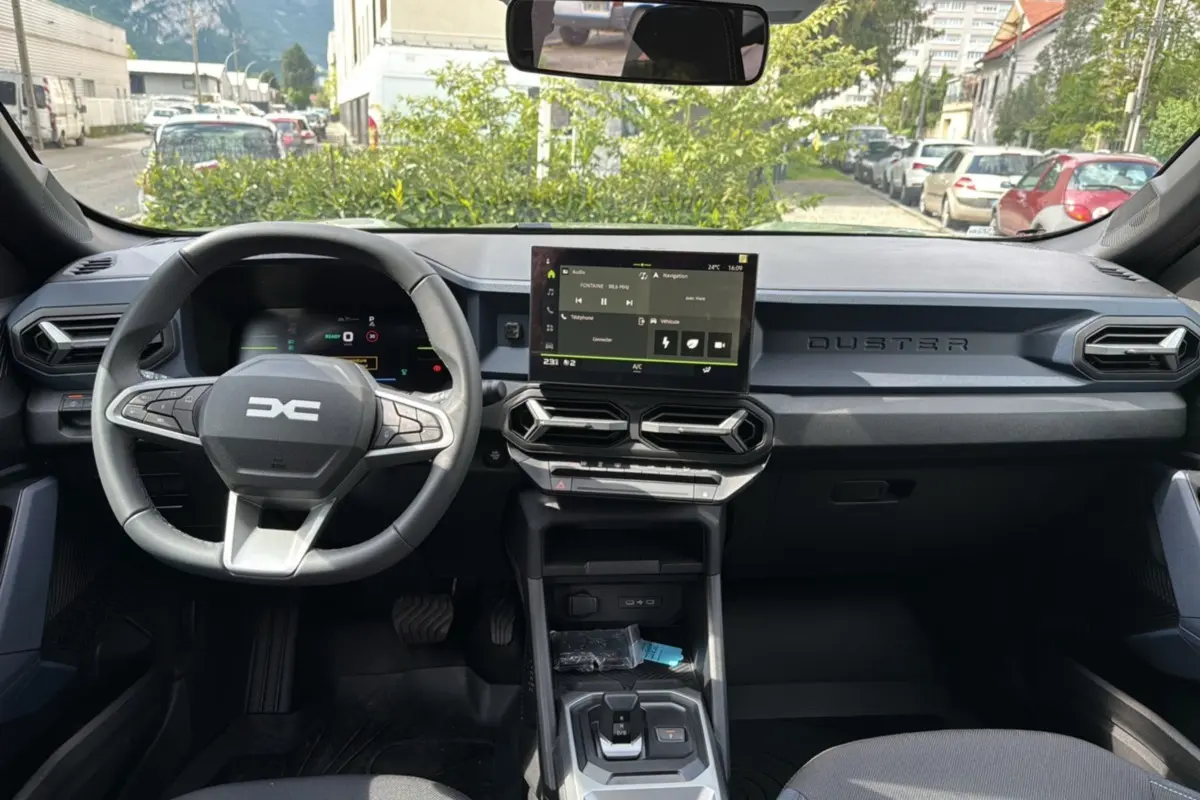 Vue intérieure frontale du tableau de bord du Dacia Duster 2025, avec écran tactile central et volant cuir noir.