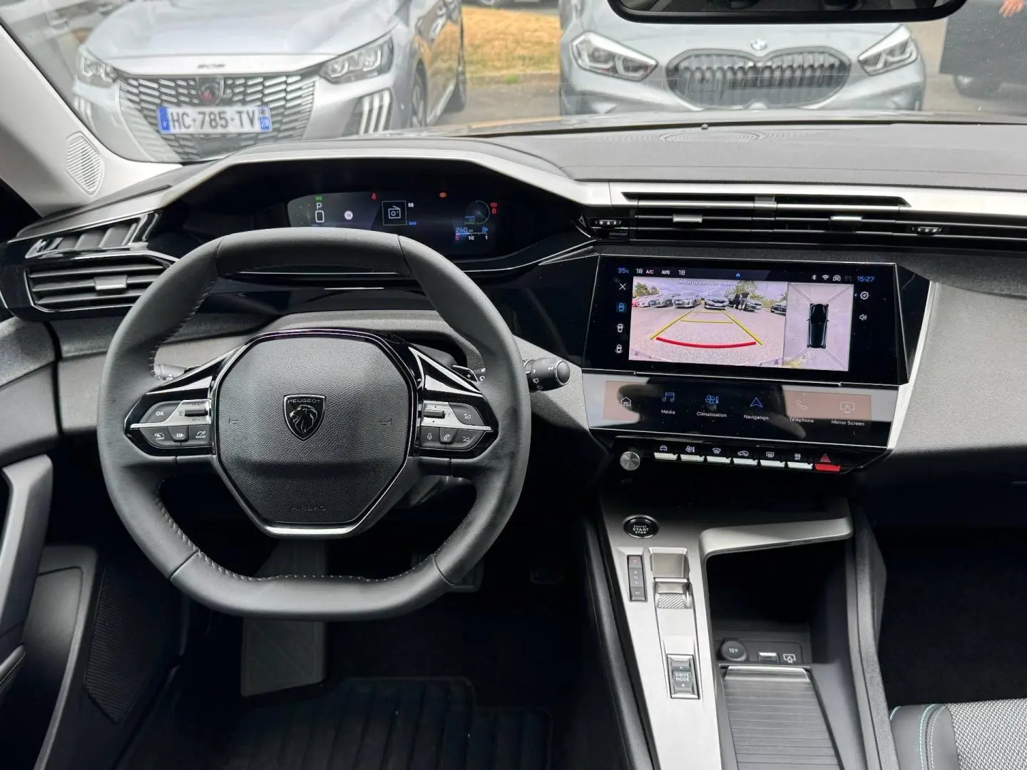 Vue intérieure centrée sur le volant Peugeot 308 gris Artense, avec tableau de bord numérique et écran tactile affichant la caméra de recul.