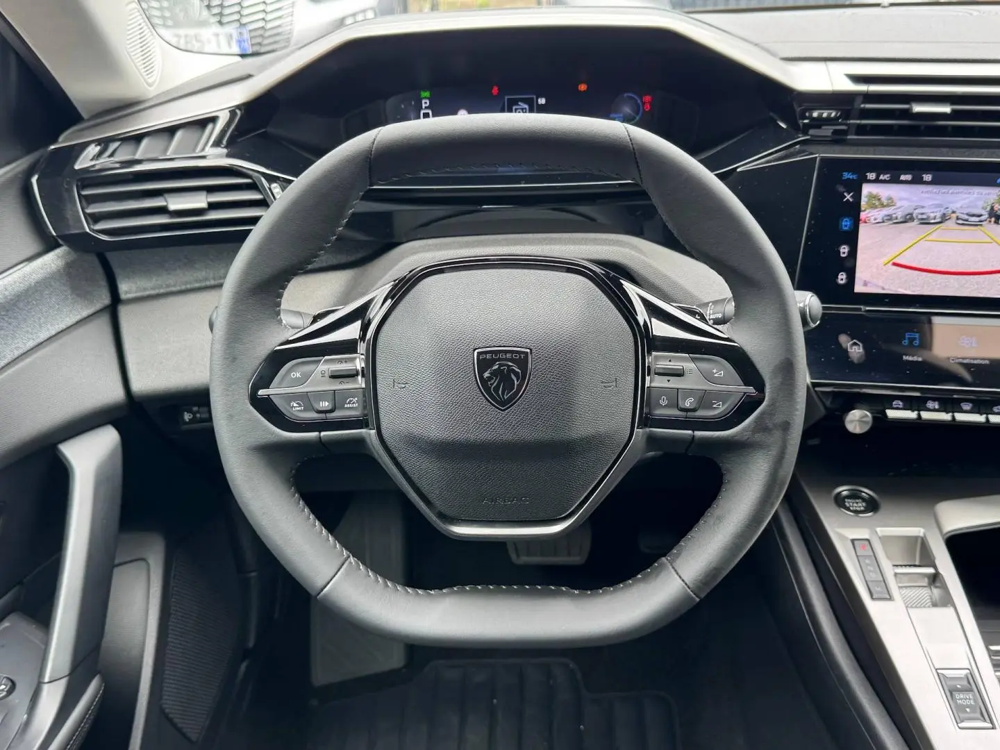 Vue rapprochée du volant multifonction Peugeot 308 2025 avec tableau de bord numérique et écran tactile de caméra de recul.