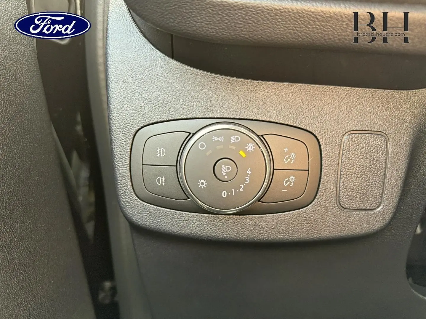 Gros plan sur le bouton de réglage des phares du Ford Puma 2023 en intérieur noir texturé.