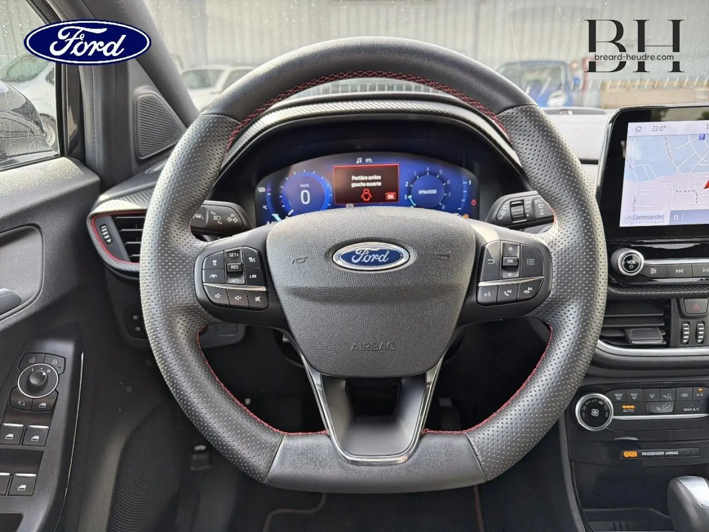 Vue intérieure centrée sur le volant perforé avec surpiqûres rouges du Ford Puma 2023, tableau de bord numérique et écran tactile visible.