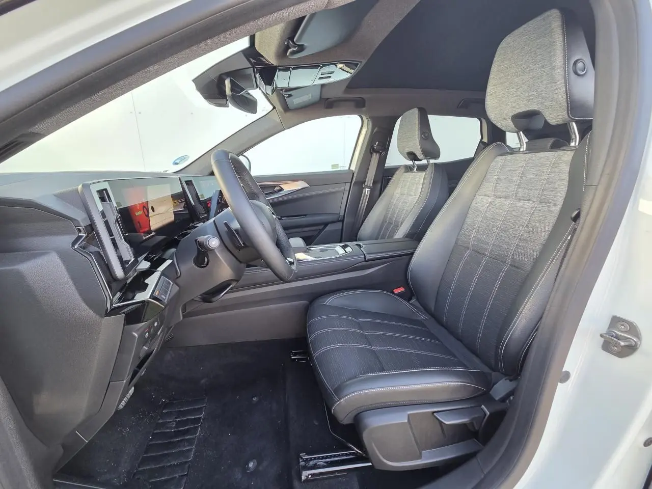 Vue intérieure côté conducteur du Renault Austral 2025 blanc nacré, sièges tissu et cuir noir, toit panoramique visible.