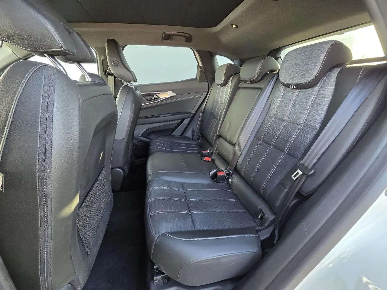 Vue latérale intérieure montrant la banquette arrière en cuir noir et tissu gris du Renault Austral 2025 blanc nacré.