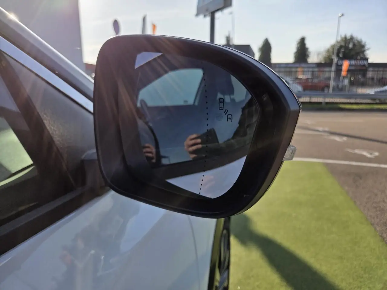 Rétroviseur extérieur droit noir sur Renault Austral blanc nacré, avec détection d'angle mort visible au soleil.