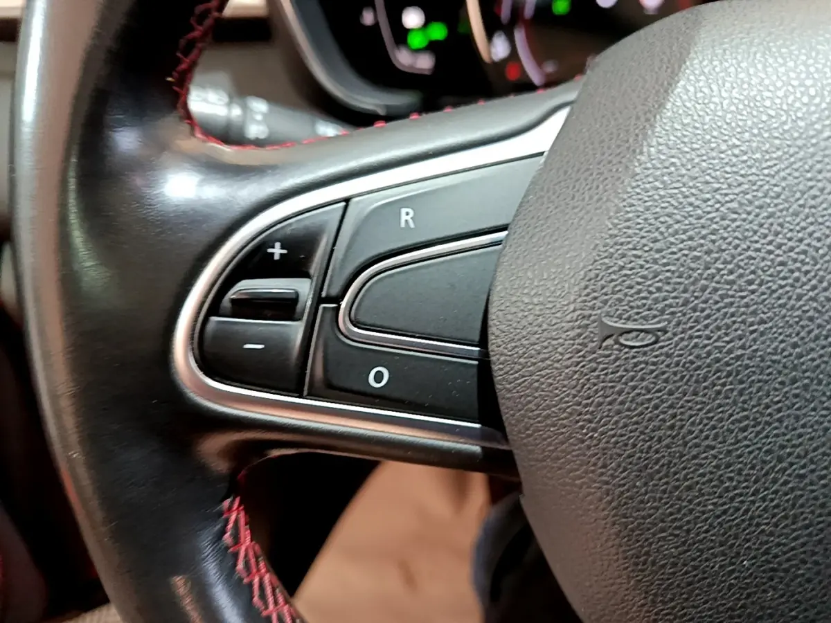 Gros plan sur les commandes de régulateur de vitesse au volant cuir noir avec surpiqûres rouges du Renault Kadjar rouge.