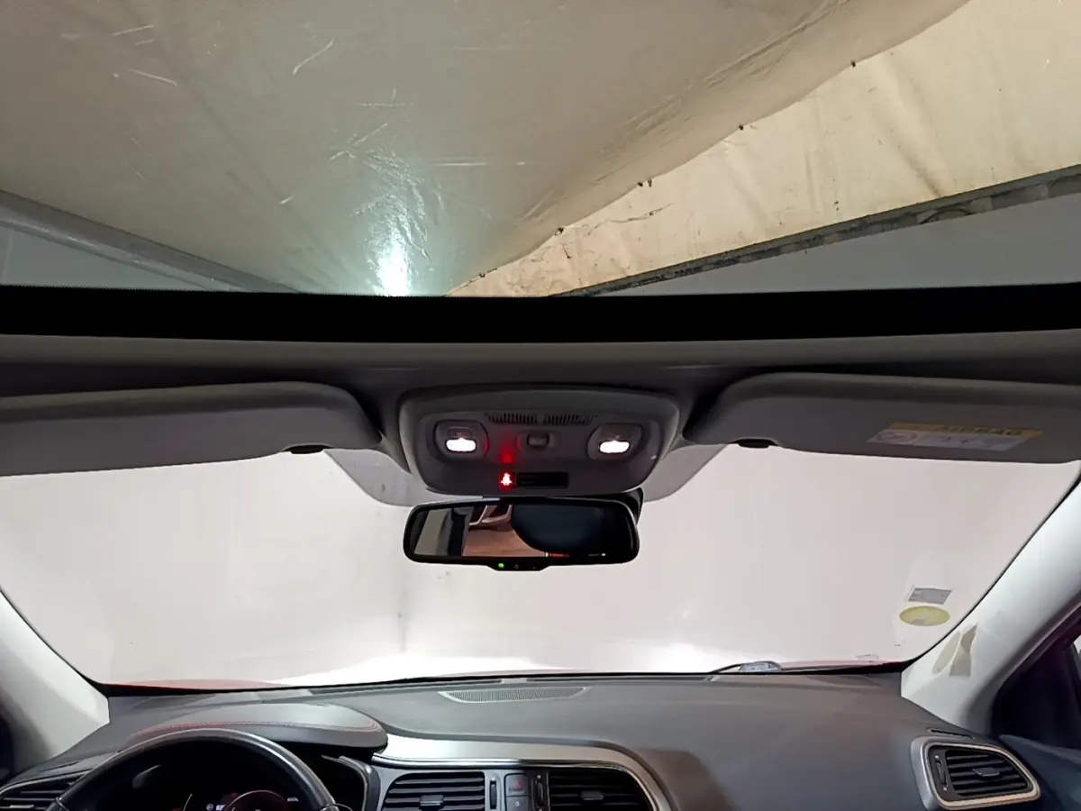Vue intérieure frontale du tableau de bord et du rétroviseur d’un Renault Kadjar rouge avec toit ouvrant panoramique.